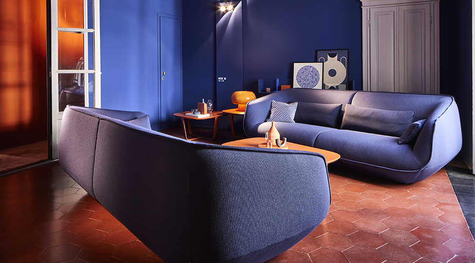 zwei Nook Sofas in Blaugrau stehen sich in blau gestrichenem Wohnzimmer gegenüber, kupferroter Fliesenboden und weiße Doppeltüre links im Bild.