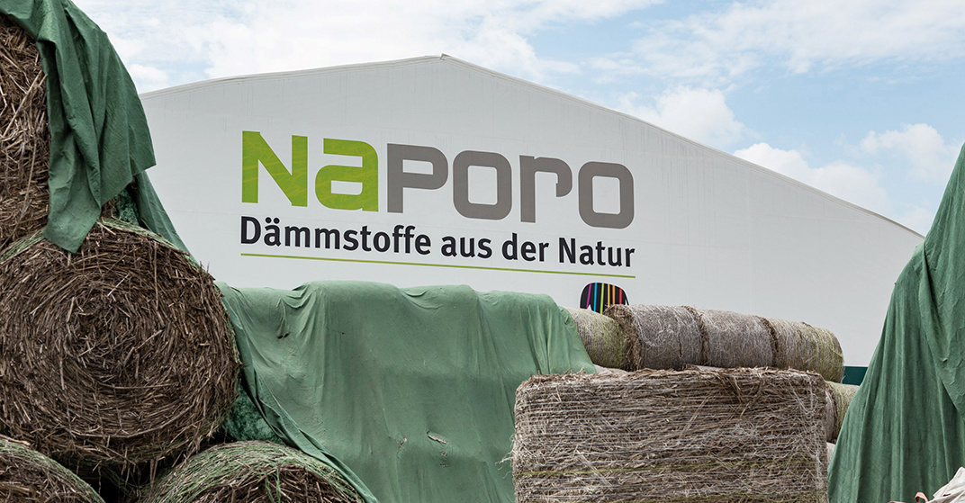 bewölkter Himmel, Gebäude mit Logo-Schriftzug der Firma Naporo drauf, im Vordergrund große Ballen an gerolltem Dämmmaterial, ökologisch.