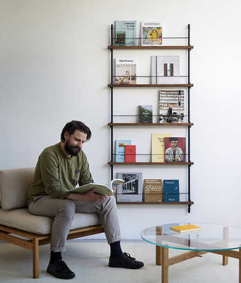 Junger Mann sitzt vor Zeitschriftenregal Magazine Shelving von Moebe und liest Zeitschrift