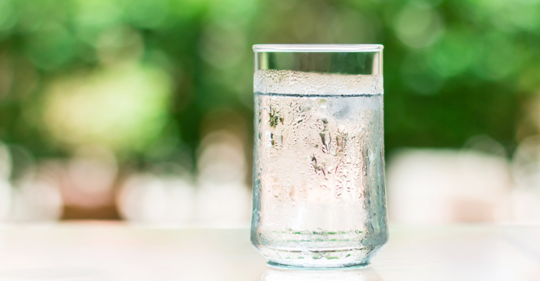 Trinkgenuss: ein beschlagenes Glas mit klarem, frischem Wasser steht auf Tisch in Gastgarten