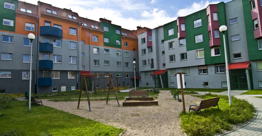 Innenhof eines typischen Gemeindebaus mit bunter Fassade, Spielplatz und Grünflächen im Vordergrund, kene Menschen