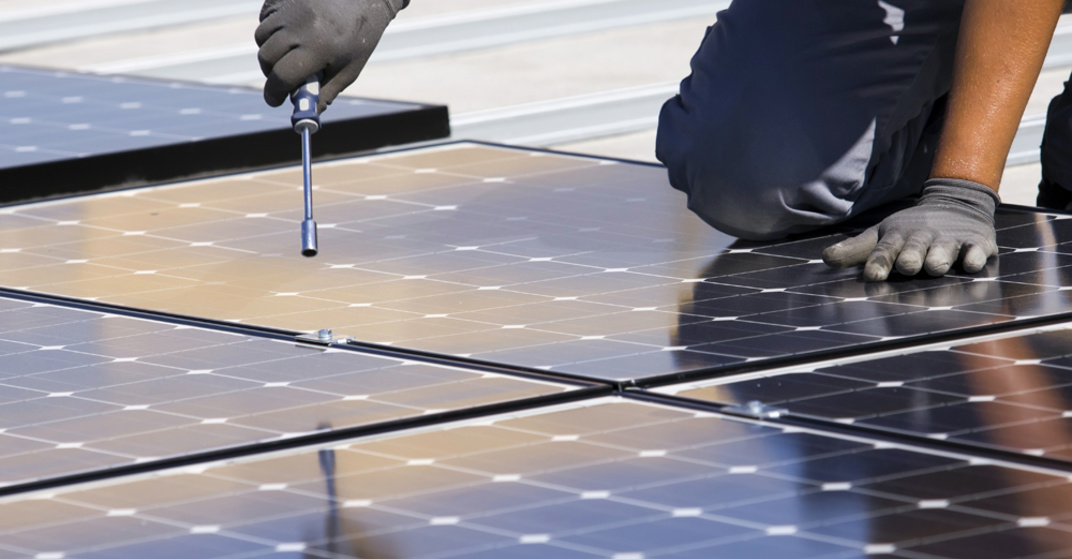 Fachmann verschraubt Photovoltaik-Paneele auf Industriedach